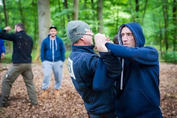 Zwei Personen üben einen Nahkampfgriff im Wald, während andere zuschauen