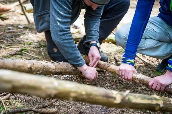 Zwei Personen verbinden Holzstücke mit Schnur im Wald