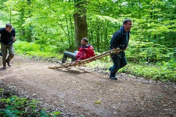 Zwei Personen ziehen eine improvisierte Trage durch den Wald