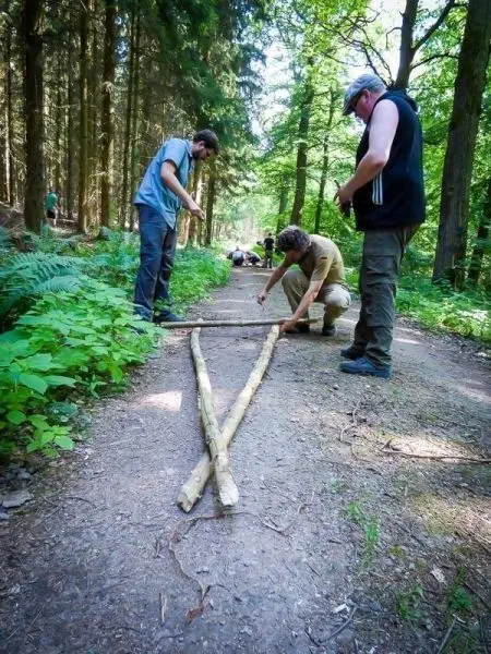 Drei Personen arbeiten an einer selbstgebauten Konstruktion aus zwei Holzstücken im Wald