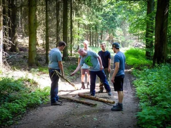Gruppe von fünf Personen betrachtet Holzstücke im Wald beim Überlebenstraining