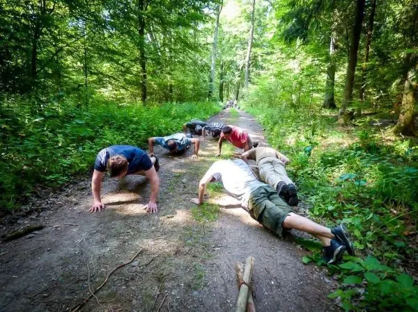 Gruppentraining mit Liegestützen auf einem Waldweg zwischen Bäumen und Sträuchern