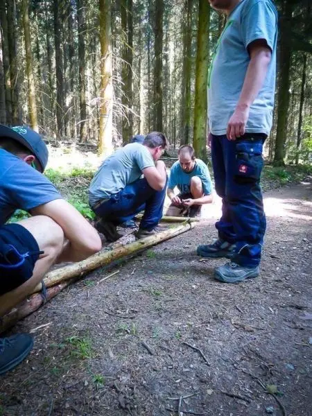 Gruppierung arbeitet an einem Holzstück im Wald, konzentriert auf eine Technik
