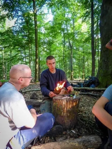 Kleines Bodenfeuer auf einem Baumstumpf, Teilnehmer beobachten aufmerksam