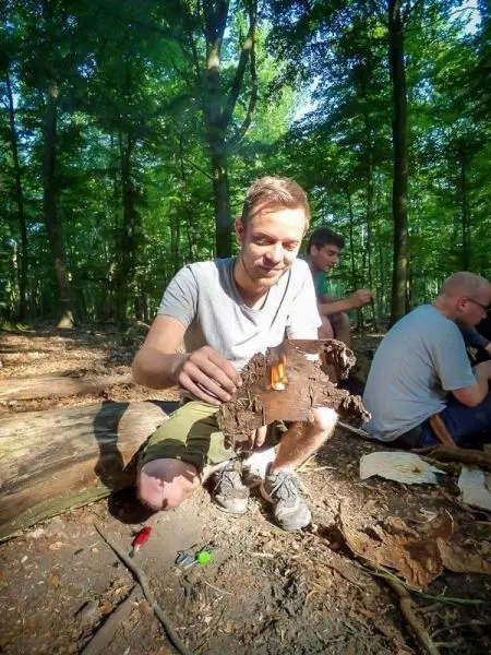 Kleines Bodenfeuer auf Rinde, während jemand Zunder hält