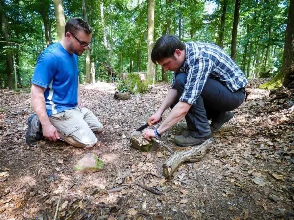 Mann bearbeitet Holzstück mit einem Messer auf dem Waldboden