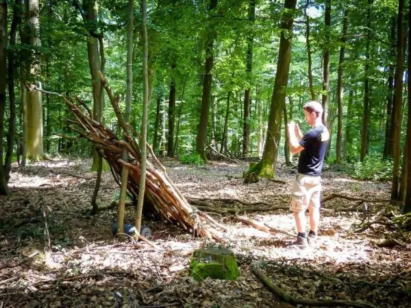 Mann fotografiert selbstgebaute Laubhütte im Wald