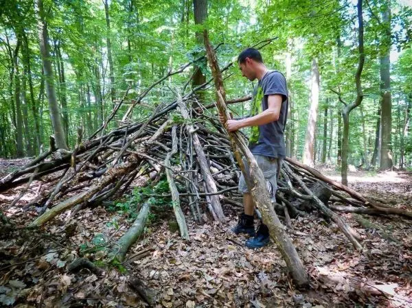 Mann konstruiert eine Laubhütte aus Ästen im Wald