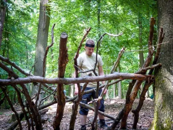Mann steht vor einer selbstgebauten Holzstruktur im Wald