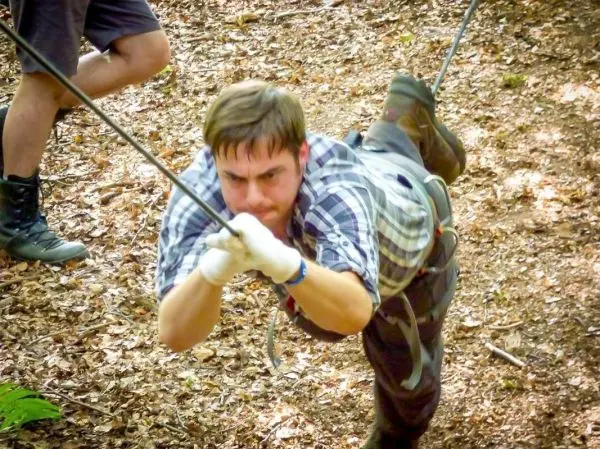 Mann überquert eine selbstgebaute Seilbrücke im Wald