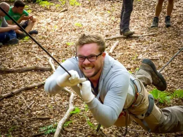 Mann überquert selbstgebaute Seilbrücke mit Seil und Sicherheitsausrüstung