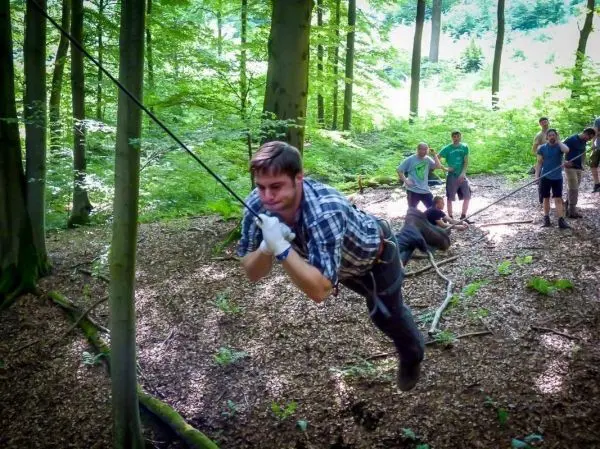 Mann überquert selbstgebaute Seilbrücke zwischen Bäumen im Wald