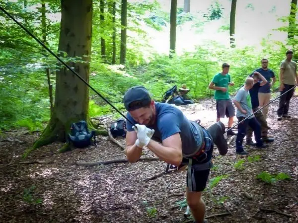 Mann überquert selbstgebaute Seilbrücke zwischen Bäumen im Wald