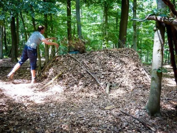 Mann wirft Laub auf eine große Laubhütte im Wald