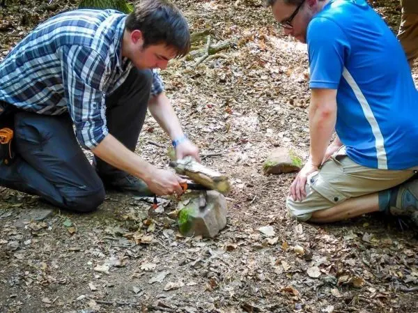 Messer schlägt auf einen Holzstock, während zwei Personen knien
