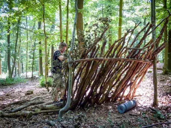 Person baut eine Struktur aus Ästen im Wald beim Survival Training