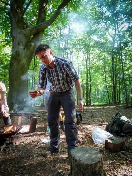 Person hält ein Stück Essen über einem Grill im Wald