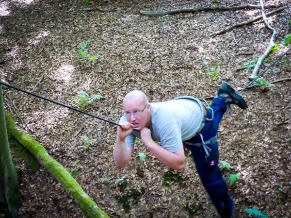 Person hängt an einem Seil zwischen Bäumen im Wald