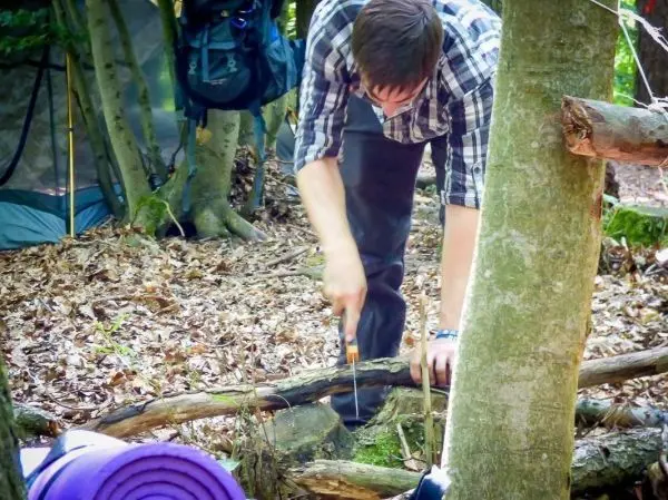 Person sägt einen Ast im Wald beim Überlebenstraining
