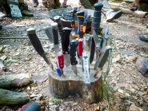 Verschiedene Messer und Werkzeuge stehen auf einem Baumstumpf im Wald