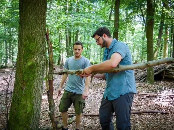 Zwei Personen arbeiten an einer selbstgebauten Konstruktion aus Ästen im Wald