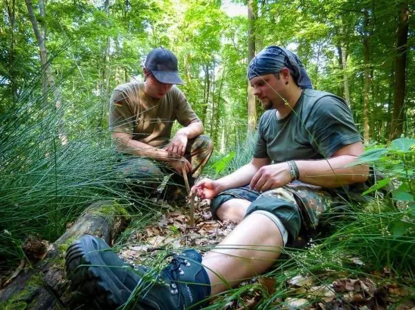 Zwei Personen sitzen im Wald und bearbeiten einen Stock mit einem Messer