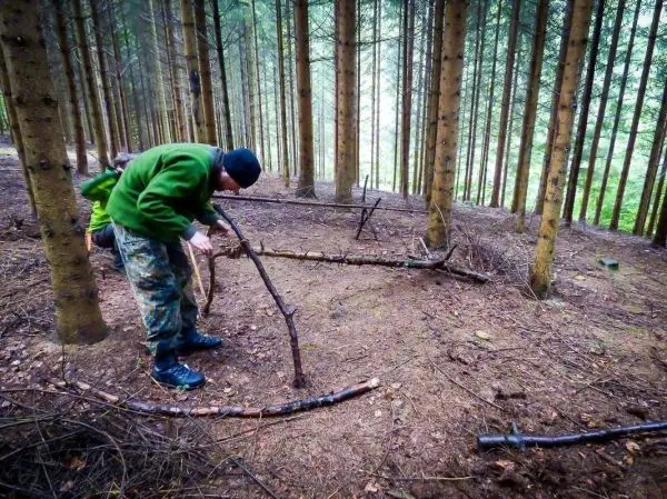 Mann formt mit einem Stock eine Konstruktion aus Ästen im Wald