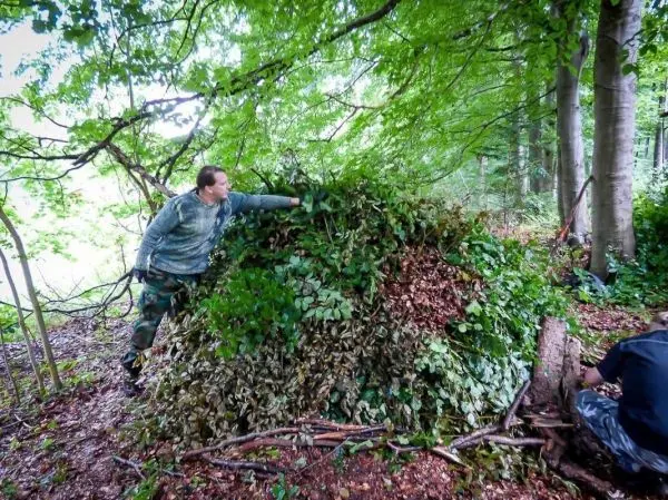 Mann platziert Äste und Blätter auf einer improvisierten Deckung im Wald