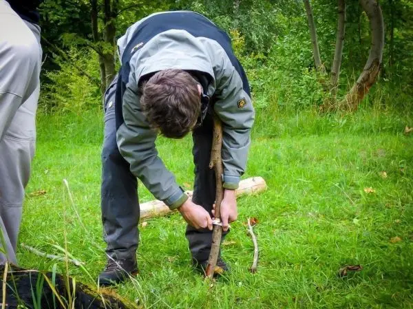 Messer schneidet Kerbe in einen Holzstock auf grünem Gras