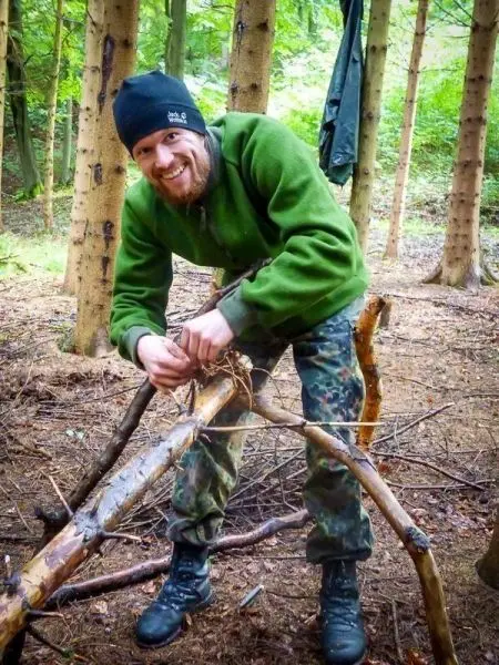 Person baut eine Struktur aus Ästen im Wald beim Survival Training