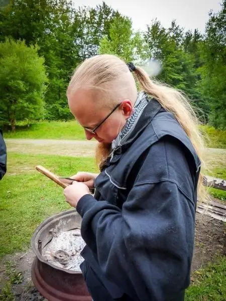 Person bearbeitet einen Holzstock im Freien beim Überlebenstraining