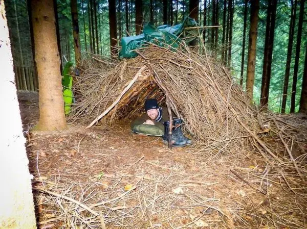 Person sitzt in einer selbstgebauten Unterkunft aus Ästen im Wald