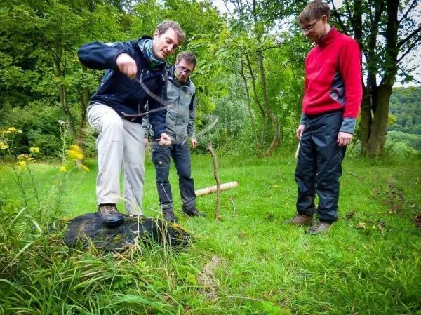 Person steht auf einem Stein und zeigt auf den Boden beim Überlebenstraining