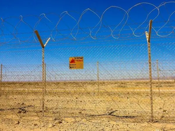 Drahtzaun mit Stacheldraht und Warnschild in einer trockenen Landschaft