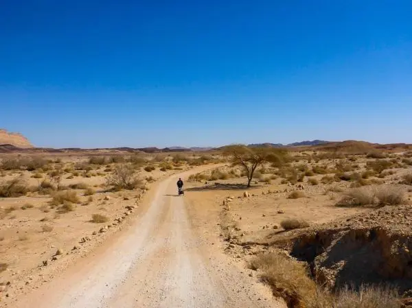 Ein Wanderer geht auf einer staubigen Straße durch eine trockene Landschaft