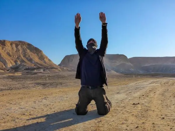 Kniende Person mit erhobenen Händen in einer trockenen, felsigen Landschaft