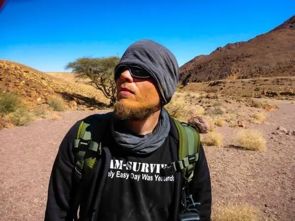 Mann mit Sonnenbrille und Kopfbedeckung steht in einer trockenen Landschaft