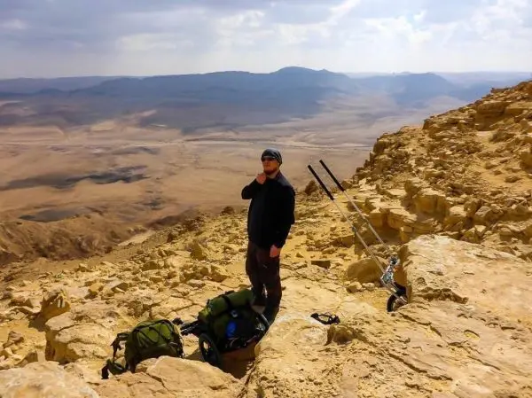 Mann steht auf einem Felsen mit Rucksack und Wanderstöcken in der Wüste