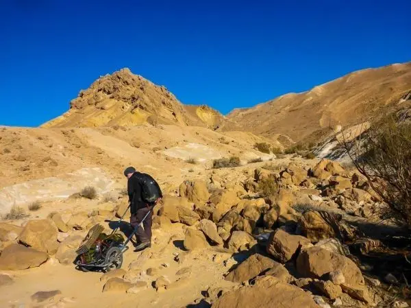 Mann zieht einen Handwagen über einen steinigen Weg in einer Wüstenlandschaft