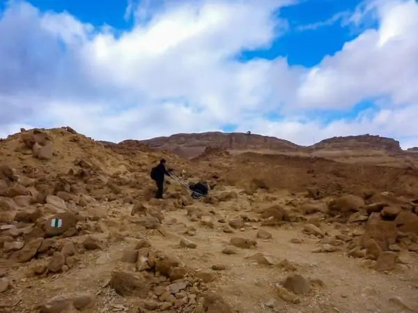 Person zieht einen Wagen über steinigen Untergrund in einer felsigen Landschaft