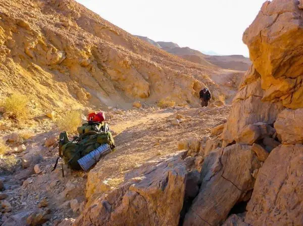 Rucksack liegt auf dem Boden, Wanderer bewegt sich durch felsige Landschaft