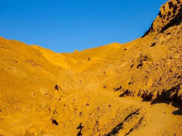 Schmaler Pfad führt durch eine steinige, gelbe Landschaft mit Hügeln