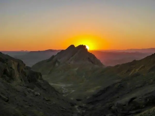 Sonnenaufgang hinter einem Gebirgskamm in einer weiten, felsigen Landschaft