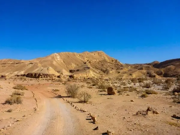 Staubiger Weg führt durch eine trockene, bergige Wüstenlandschaft unter klarem Himmel