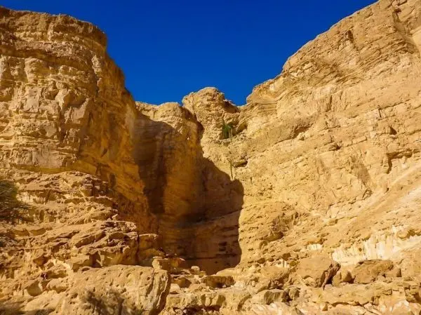 Steile, sandfarbene Felsen mit Schatten und klarem blauen Himmel