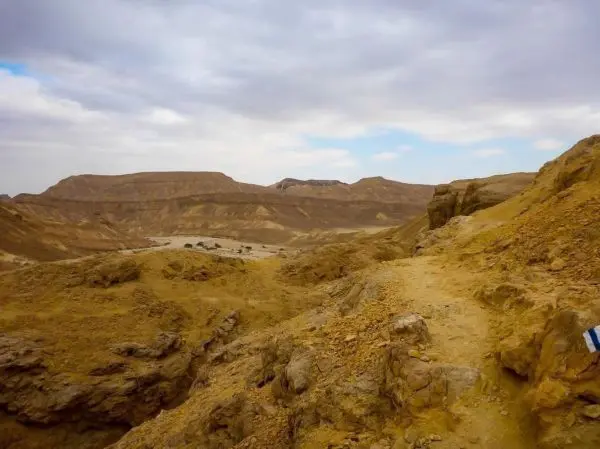 Steiniger Pfad führt durch eine trockene, hügelige Landschaft unter bewölktem Himmel