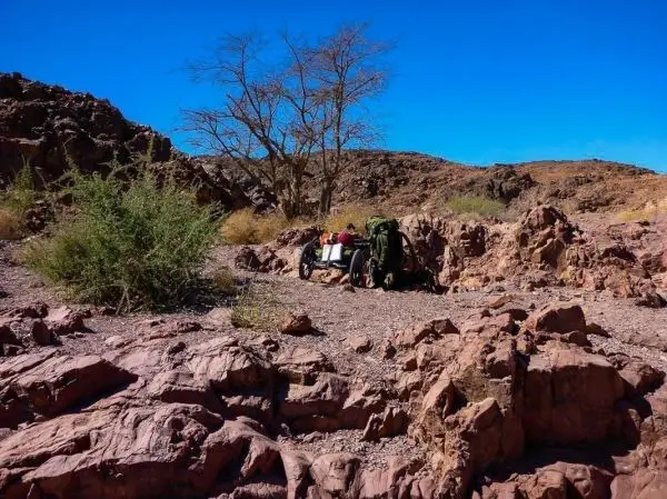 Wagen mit Gepäck steht zwischen Felsen und Sträuchern in einer trockenen Landschaft