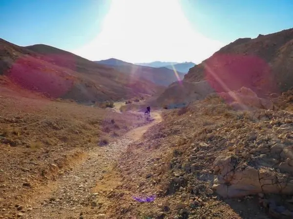 Wanderer auf einem schmalen Pfad zwischen steinigen Hügeln in einer trockenen Landschaft