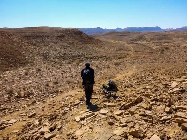 Wanderer mit Rucksack zieht einen Handwagen über steinigen Weg in karger Landschaft