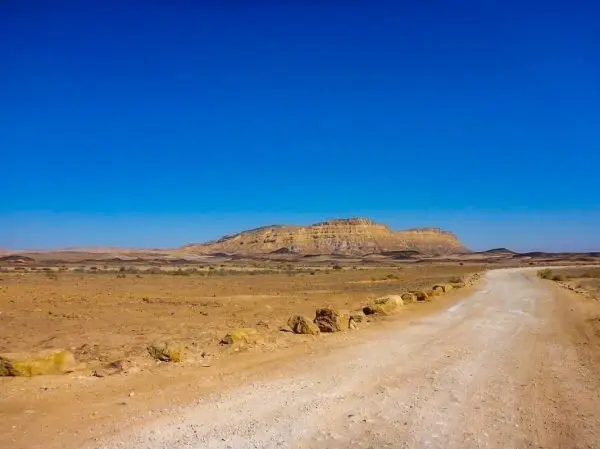 Wüstenlandschaft mit einer unbefestigten Straße und einem Hügel im Hintergrund